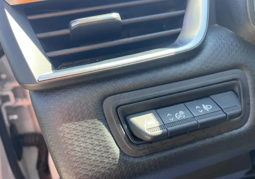 Gros plan sur les commandes de réglage des aides à la conduite et éclairage dans l’habitacle de la Renault Clio blanc Quartz.