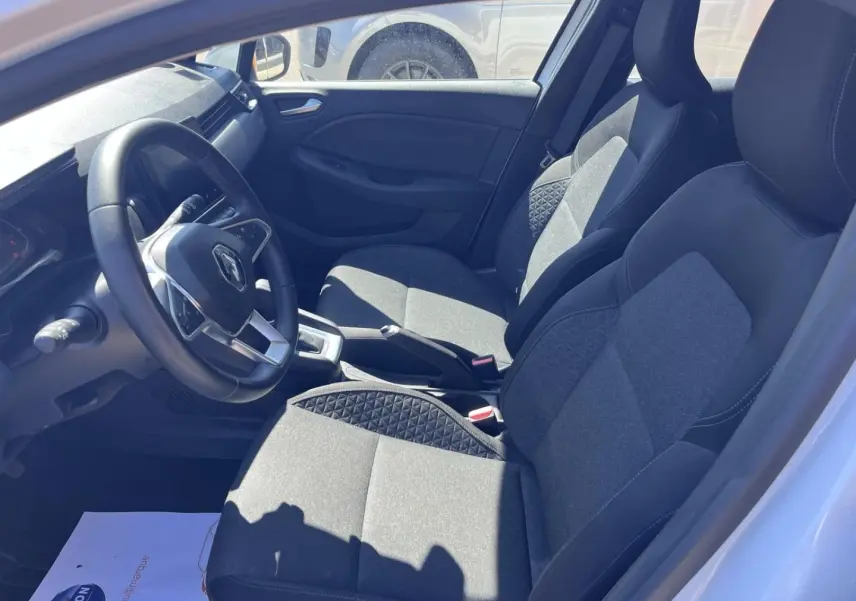 Vue intérieure côté conducteur de la Renault Clio blanc quartz, sièges tissu noir avec surpiqûres et volant multifonction.