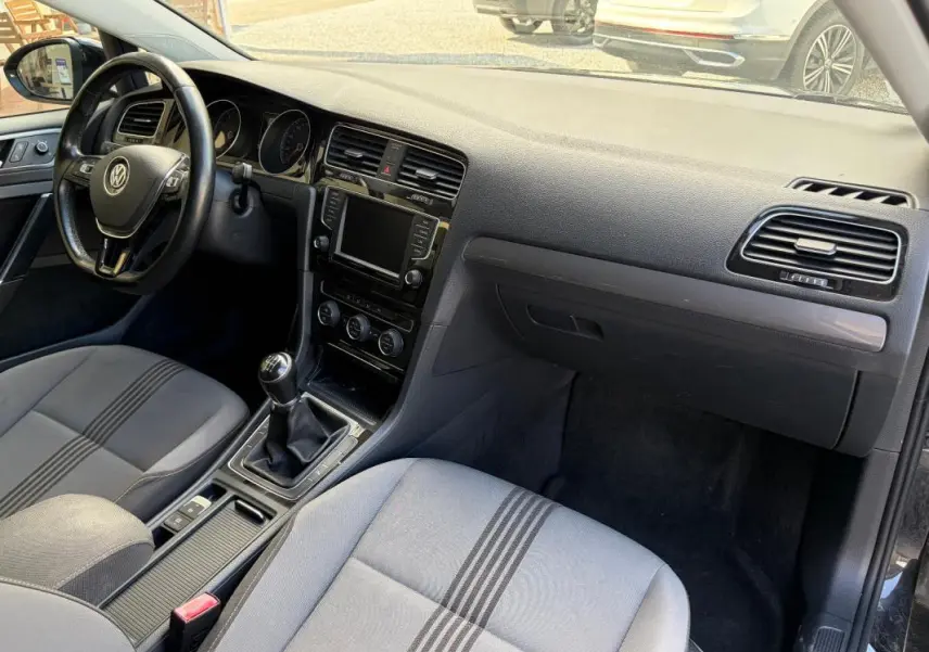 Vue intérieure côté conducteur de la Volkswagen Golf 7 noire, volant cuir multifonctions et boîte manuelle visibles.