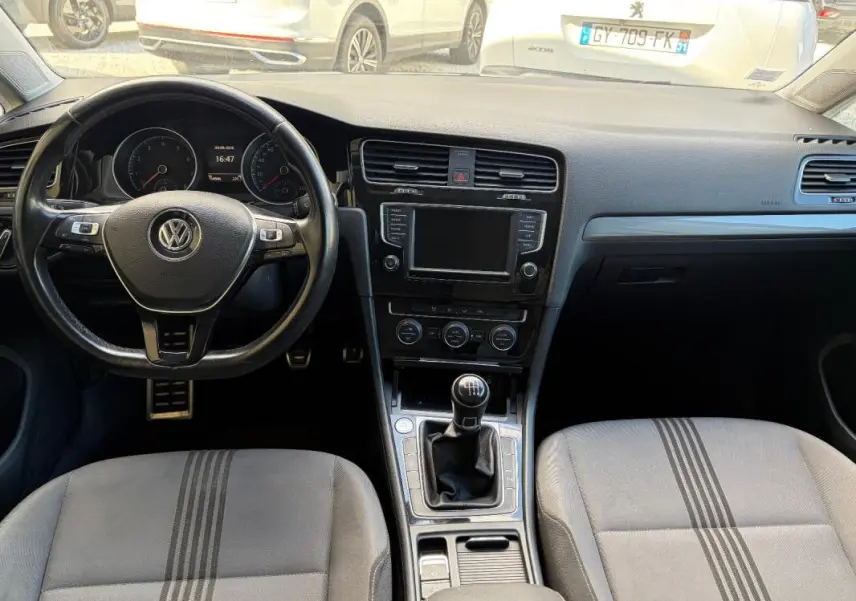 Vue intérieure avant de la Volkswagen Golf 7 noire, volant cuir multifonctions et levier de vitesse manuel visibles.