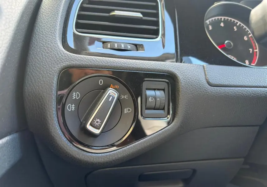 Gros plan sur le bouton de commande des phares et la molette de réglage de l’éclairage dans l’habitacle d’une Volkswagen Golf noire.