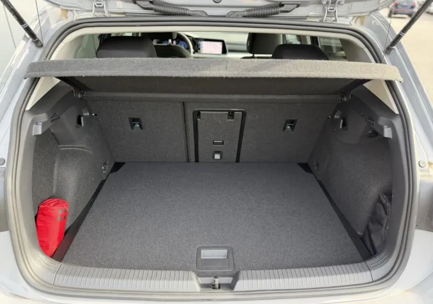 Coffre ouvert d'une Volkswagen Golf 8 gris lunaire, montrant un espace de rangement propre avec trappe centrale et kit de secours rouge.