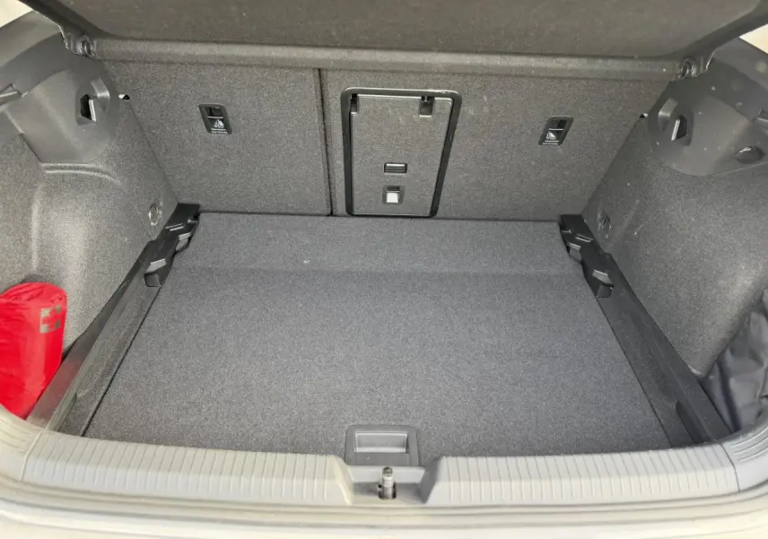 Coffre ouvert vu de face de la Volkswagen Golf 8 gris lunaire, avec tapis et rangement intérieur visible.