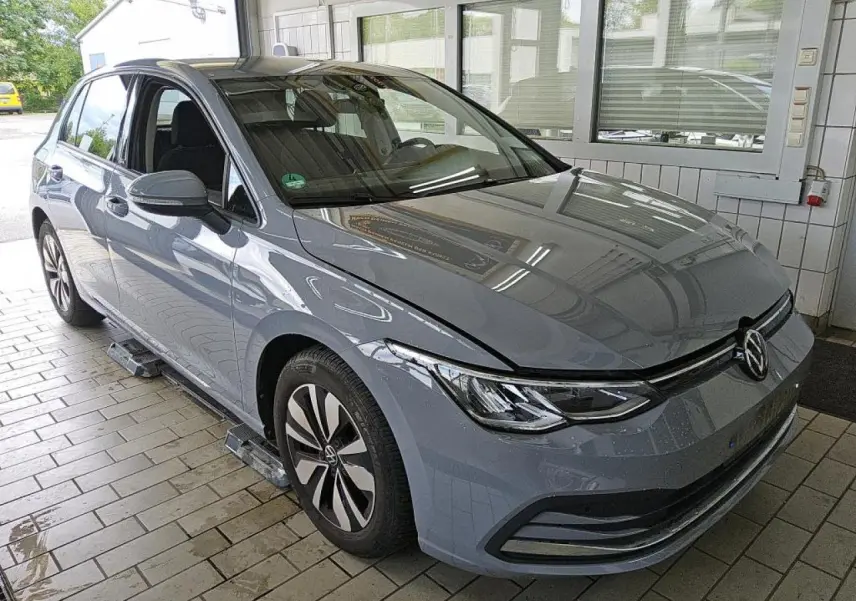 Volkswagen Golf 8 gris lunaire vue 3/4 avant droit dans un garage avec jantes alliage et phares LED.