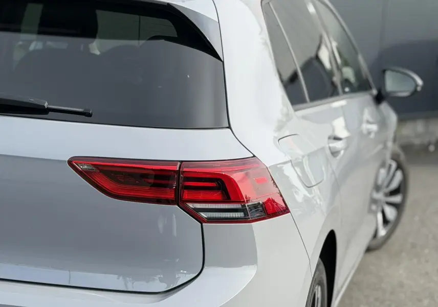 Vue arrière droite d'une Volkswagen Golf 8 gris lunaire avec feux arrière LED et jantes alliage visibles.