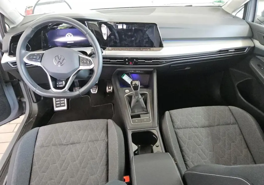 Vue intérieure frontale de la Volkswagen Golf 8 avec tableau de bord digital et volant multifonction en cuir noir.