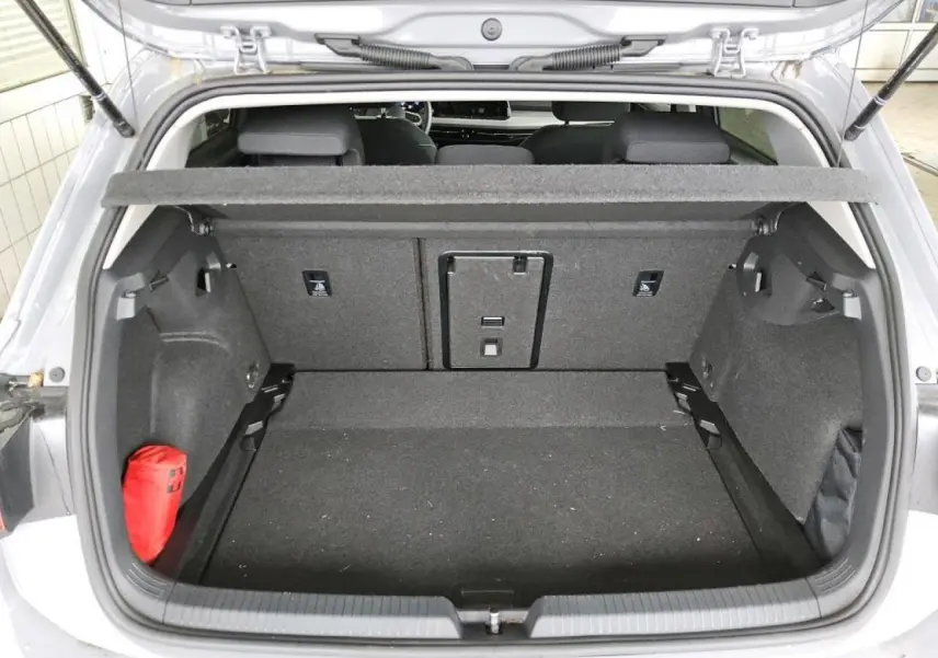 Coffre ouvert vu de l'arrière d'une Volkswagen Golf 8 gris lunaire, avec cache-bagages et trousse de secours rouge.