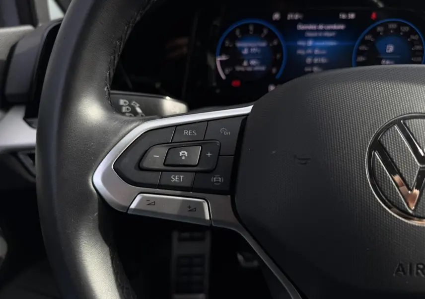 Gros plan sur le volant multifonction cuir de la Volkswagen Golf 8 gris lunaire, avec commandes de régulateur et tableau de bord numérique flou.