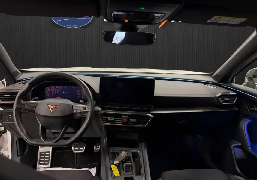 Vue intérieure avant du tableau de bord noir du CUPRA Formentor blanc 2024 avec écran tactile central et volant multifonction.