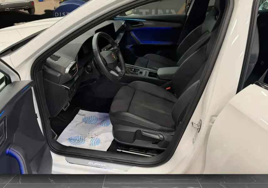 Vue intérieure côté conducteur d'un CUPRA Formentor blanc 2024, sièges noirs et éclairage d'ambiance bleu.