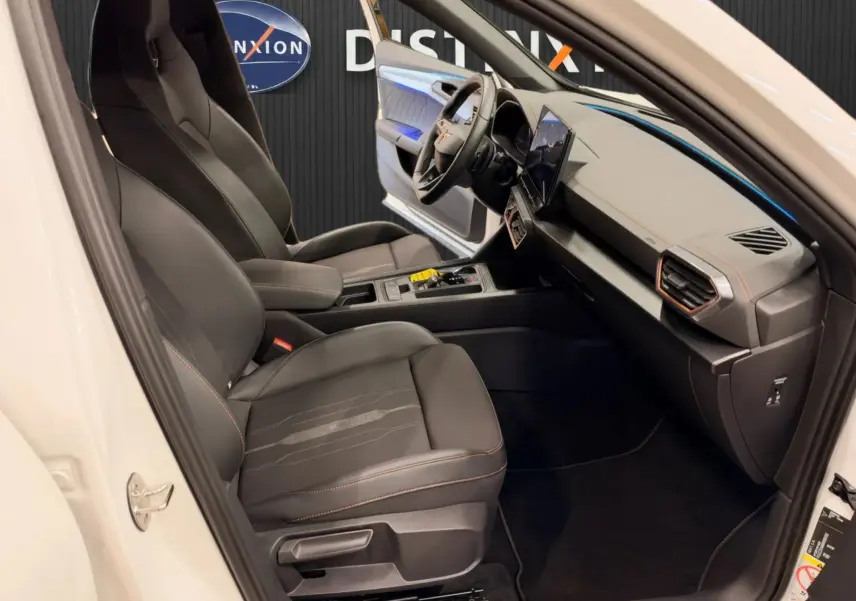 Vue intérieure côté conducteur de la CUPRA Formentor blanc 2024, sièges en cuir noir avec surpiqûres orange et tableau de bord moderne.