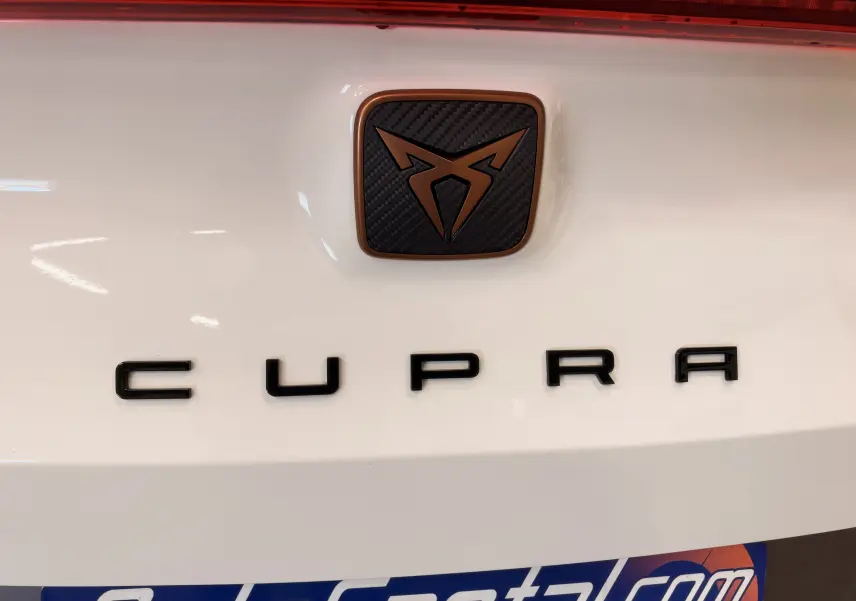 Gros plan sur le logo CUPRA noir et cuivre sur fond blanc à l'arrière du véhicule.