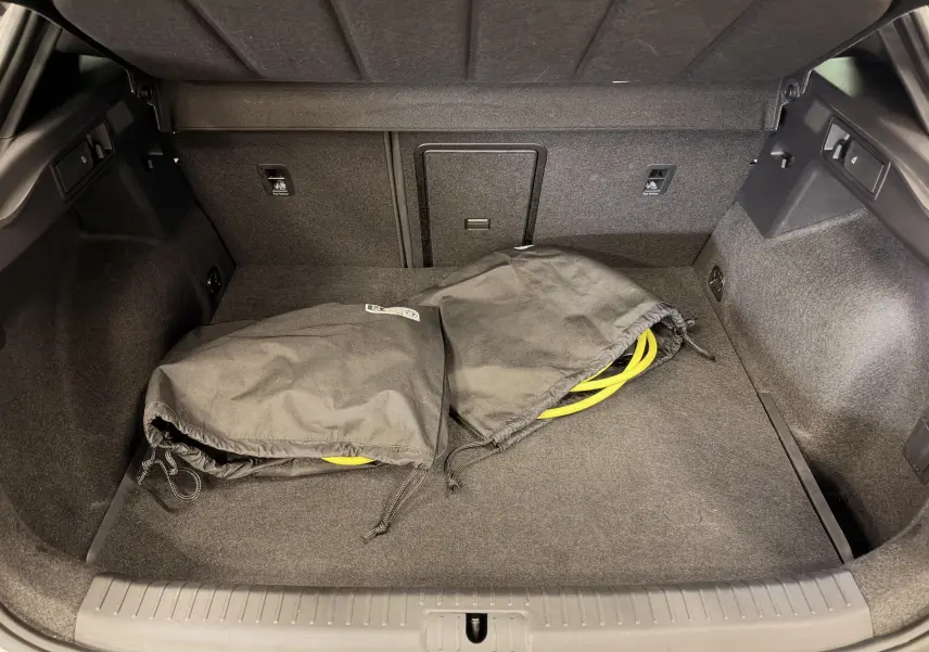 Coffre ouvert d'une CUPRA Formentor blanc 2024, montrant un intérieur noir avec deux sacs contenant des câbles jaunes.