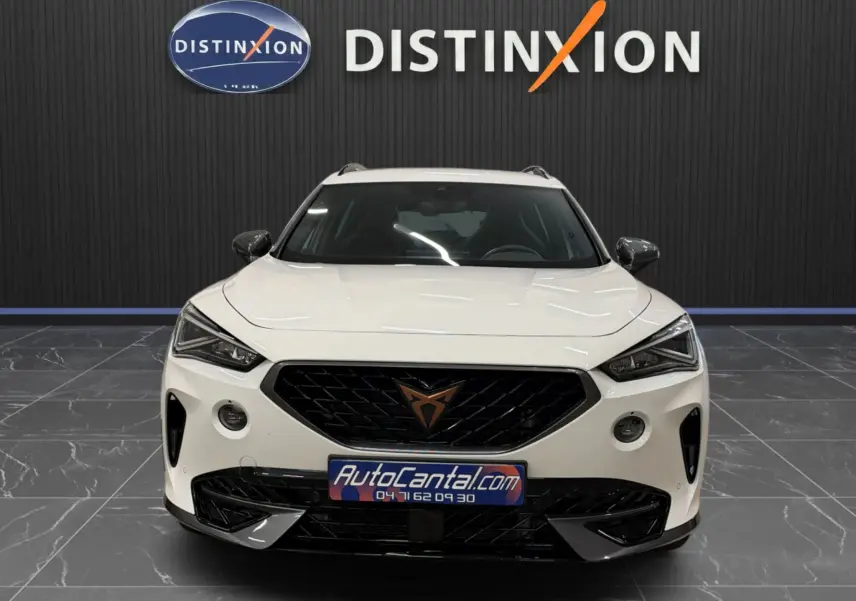 Vue frontale d'un CUPRA Formentor blanc 2024 avec calandre noire et logo cuivre, dans un showroom intérieur.