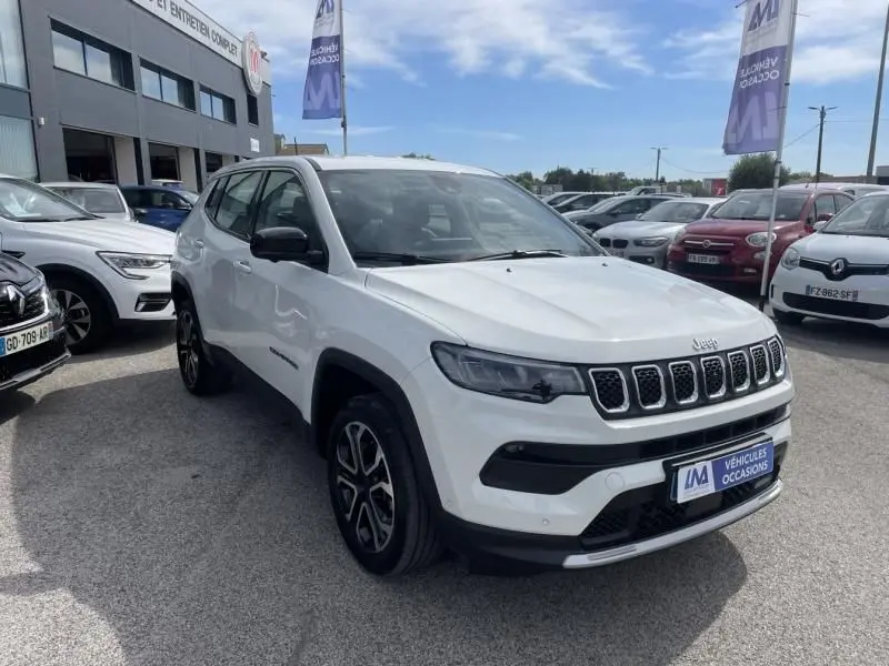 Jeep Compass blanc en 3/4 avant droit, version hybride 2024, avec calandre distinctive et jantes noires.