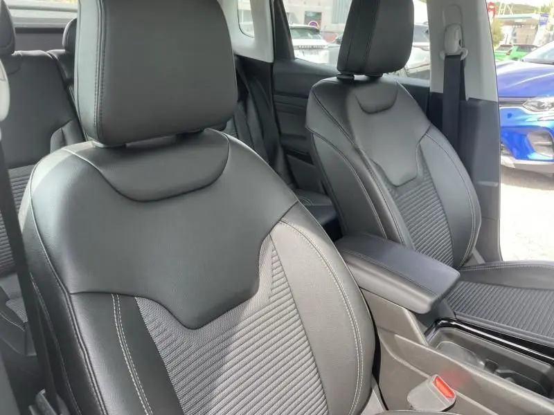 Gros plan sur les sièges avant en cuir noir du Jeep Compass 2024, version hybride essence, avec accoudoir central visible.