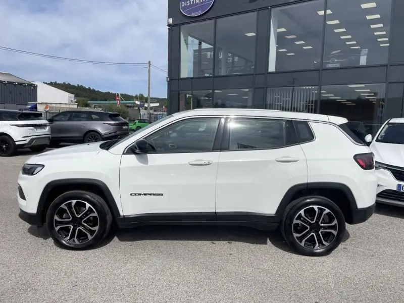 Vue de profil côté gauche d'un Jeep Compass blanc 2024 avec jantes noires et logo distinctif sur la porte