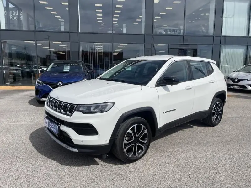 Jeep Compass blanc en 3/4 avant droit, avec jantes noires et détails noirs contrastants, stationné devant un bâtiment vitré.