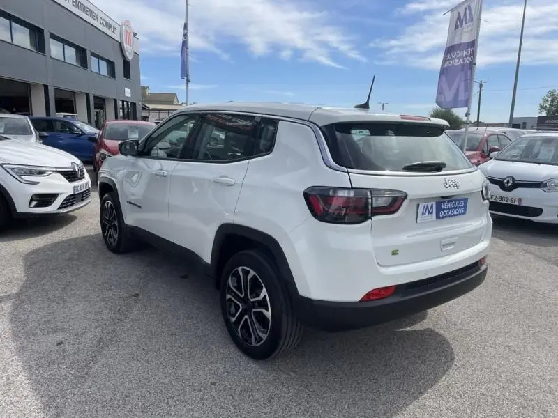 Jeep Compass blanc en 3/4 arrière droit, version hybride 2024 avec jantes alliage et feux arrière foncés.