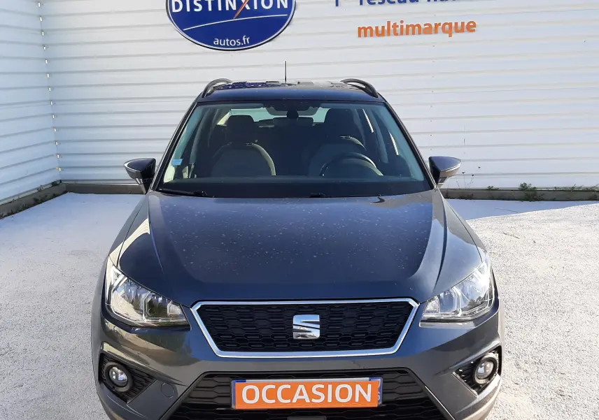 Vue de face d'un SEAT Arona gris magnetic avec toit noir, affichant une plaque "OCCASION" sur un parking extérieur.