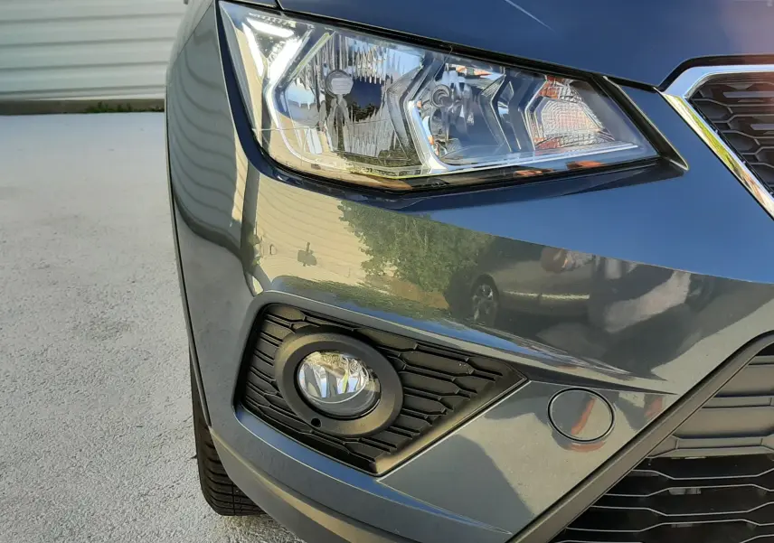 Gros plan sur l'avant droit d'une SEAT Arona gris magnetic avec phare et antibrouillard visibles.