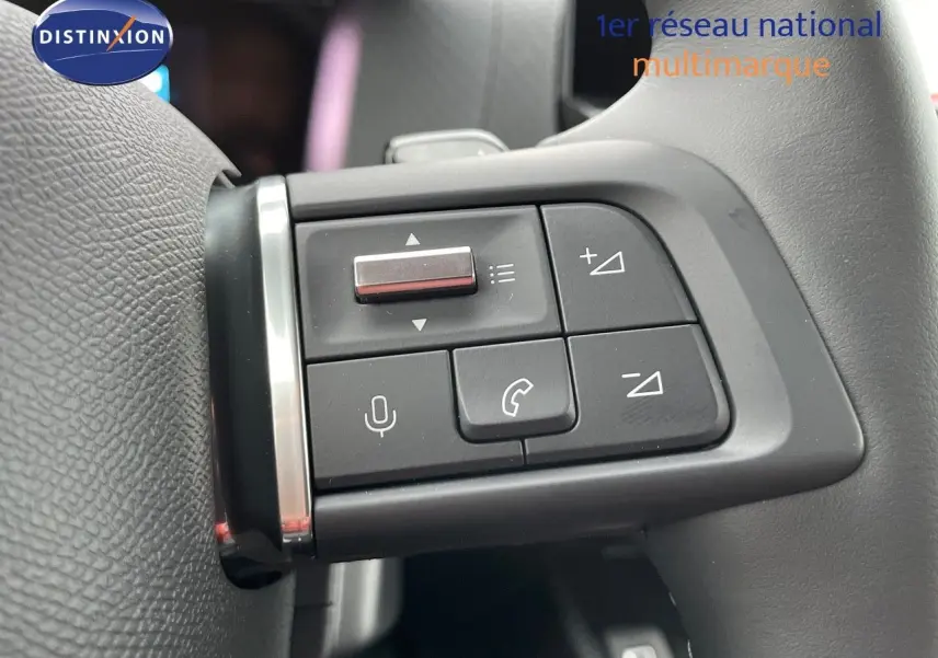 Gros plan sur les commandes multifonctions du volant noir d'une Citroën C4 gris platinium 2024.