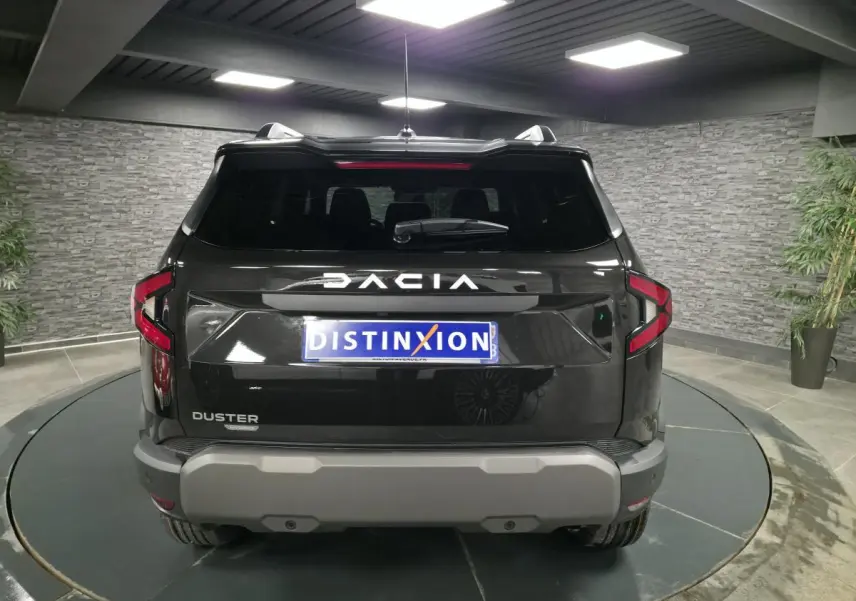 Vue arrière d'un Dacia Duster 1.6 Hybrid noir nacré avec logo DACIA lumineux et bouclier arrière gris dans un showroom.