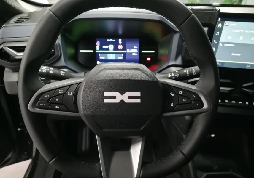 Vue rapprochée du volant noir du Dacia Duster 1.6 Hybrid 2025 avec commandes intégrées et tableau de bord digital.