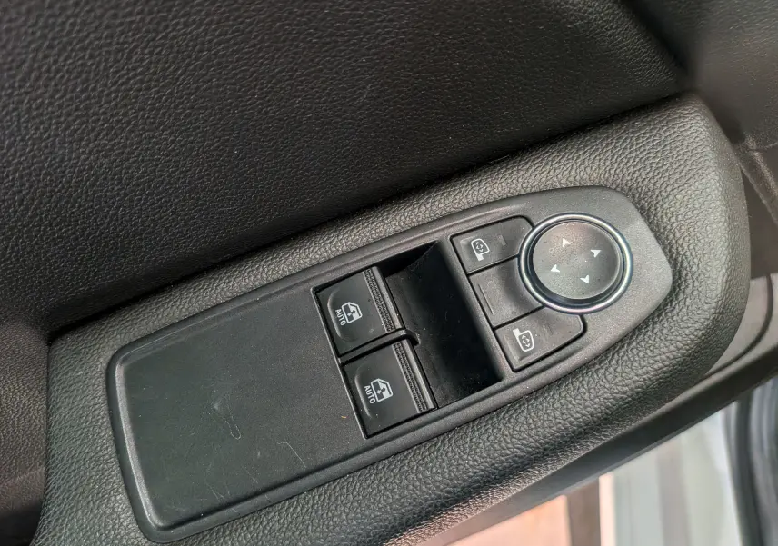 Gros plan sur les commandes des vitres électriques et des rétroviseurs sur la porte côté conducteur d’une Renault Clio V Blanc Glacier.