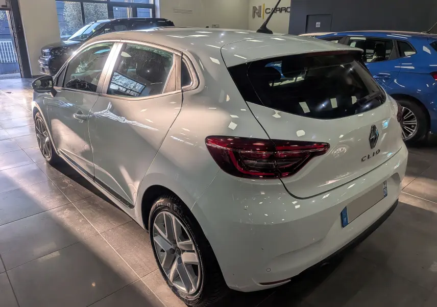Vue 3/4 arrière droite d'une Renault Clio V Blanc Glacier en intérieur, avec feux arrière LED et jantes alliage distinctives.