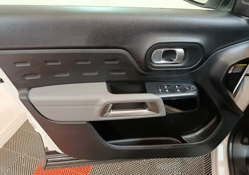 Vue rapprochée de la porte avant gauche noire et grise du Citroën C5 Aircross Hybrid 225 ë-EAT8 avec commandes de vitres et poignée métallique.