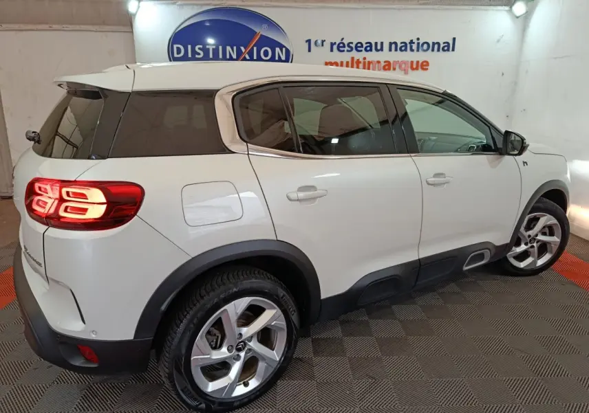 Vue 3/4 arrière droite d'un Citroën C5 Aircross Hybrid blanc avec feux arrière LED allumés en intérieur showroom.