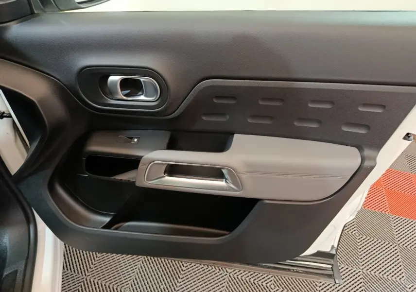 Intérieur côté gauche de la porte avant blanche du Citroën C5 Aircross Hybrid avec poignée grise et commandes vitrées.