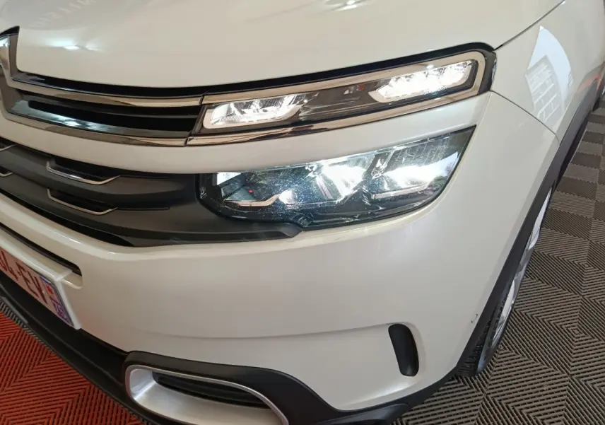Gros plan sur l'avant droit blanc du Citroën C5 Aircross Hybrid avec ses phares LED allumés et calandre chromée.