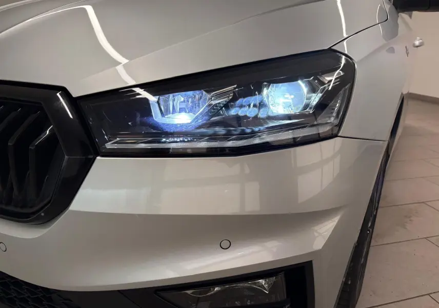 Gros plan sur le phare avant droit allumé d'une Skoda Fabia 2025 gris argent avec toit noir, version Monte Carlo.