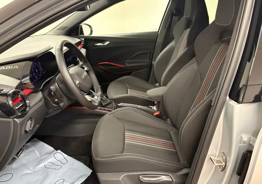 Vue intérieure côté conducteur de la Skoda Fabia 2025 avec sièges noirs à bandes rouges et détails rouges sur la porte.