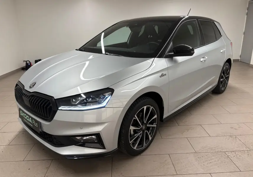 Vue 3/4 avant d'une Skoda Fabia 2025 gris argent avec toit noir et jantes noires, en intérieur sur sol carrelé.