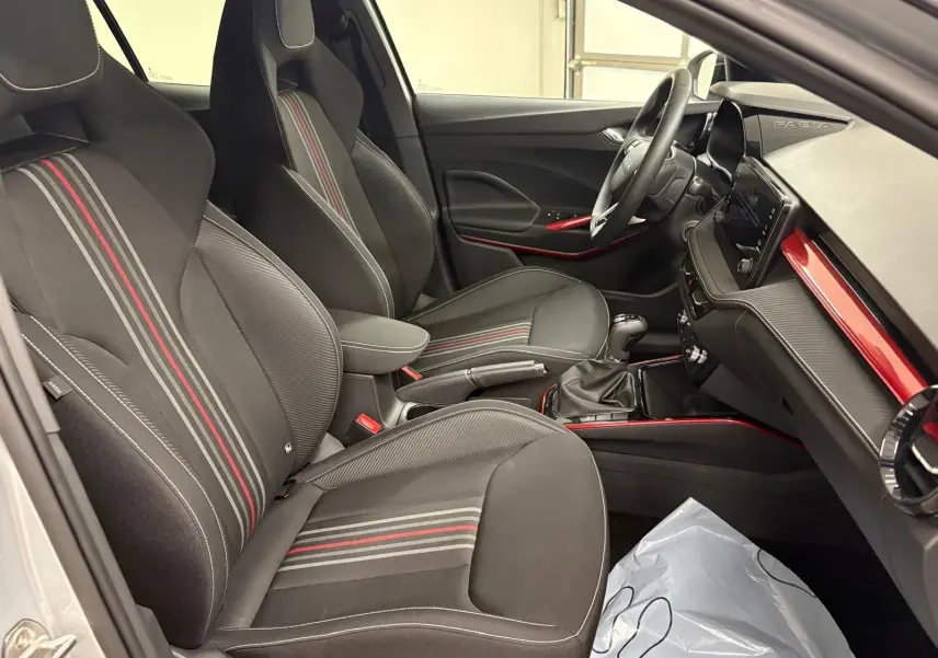 Vue intérieure côté conducteur de la Skoda Fabia 2025, sièges noirs avec bandes rouges et tableau de bord avec inserts rouges.