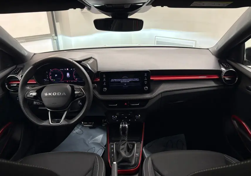 Vue intérieure avant de la Skoda Fabia 2025, tableau de bord noir avec accents rouges et volant multifonction.