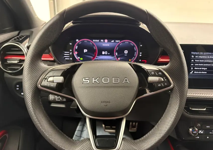 Vue centrée sur le volant perforé SKODA de la Fabia 2025 avec tableau de bord numérique et inserts rouges.