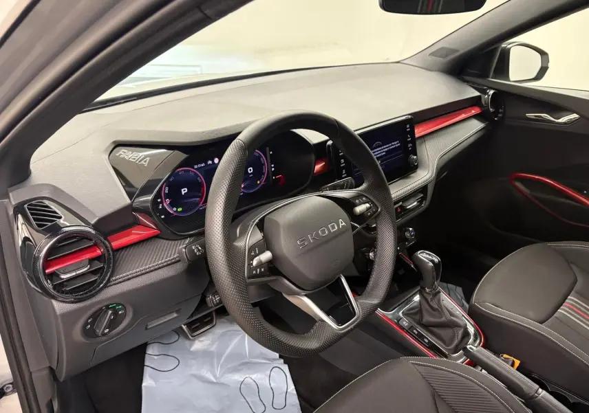 Vue intérieure côté conducteur de la Skoda Fabia 2025, tableau de bord noir avec touches rouges et volant multifonction.