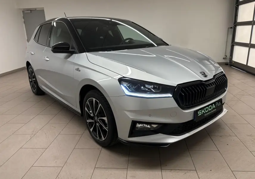 Vue 3/4 avant droite d'une Skoda Fabia 2025 gris argent avec toit noir et calandre noire distinctive.
