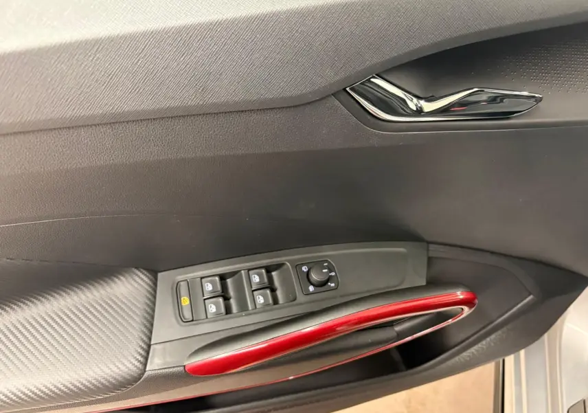 Vue intérieure du panneau de porte côté conducteur de la Skoda Fabia 2025, avec poignée rouge et commandes de vitres noires.