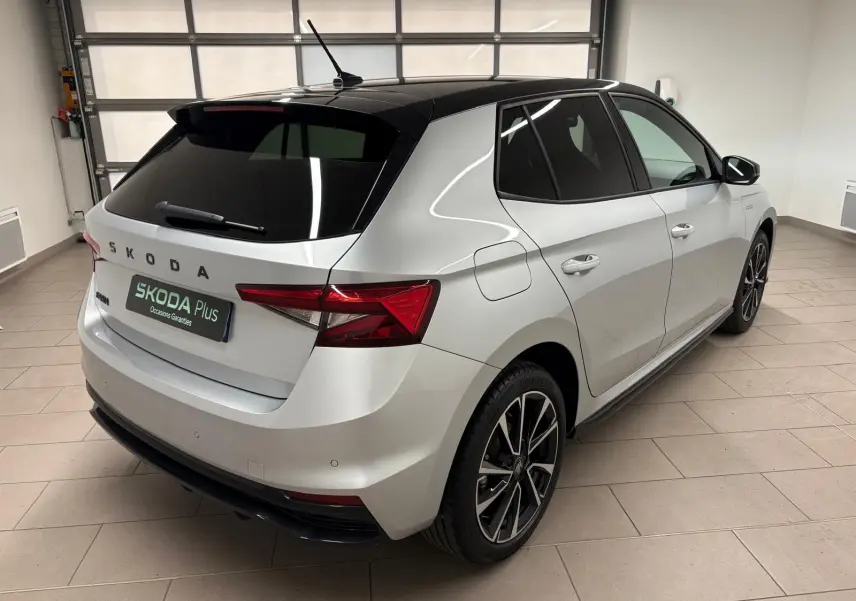 Vue 3/4 arrière droite d'une Skoda Fabia 2025 gris argent avec toit noir et jantes alliage noires en intérieur showroom.