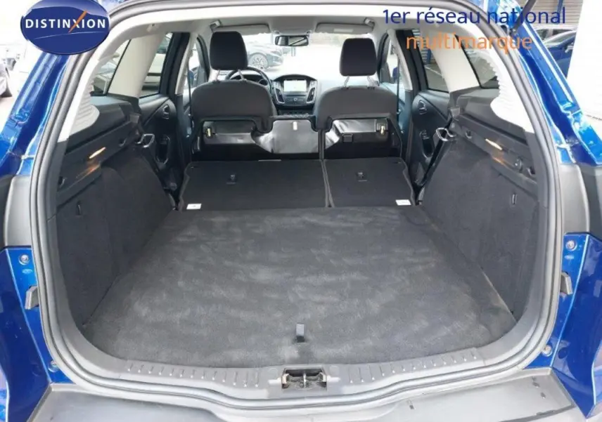 Vue arrière du coffre ouvert d'une Ford Focus SW bleu foncé, sièges arrière rabattus pour un grand espace de chargement.