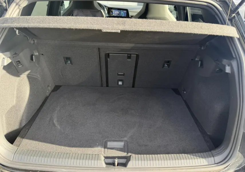 Coffre ouvert vu de l'arrière d'une Volkswagen Golf 8 noire, montrant l'espace de chargement et la tablette arrière.