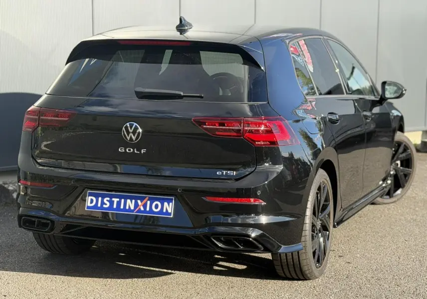 Vue 3/4 arrière droite d'une Volkswagen Golf 8 noire avec jantes noires et double sortie d'échappement R-Line.