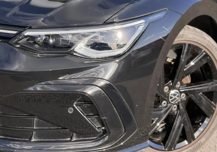 Gros plan sur l'avant droit noir brillant d'une Volkswagen Golf 8 R-Line avec phare IQ.Light et jante alliage noir.