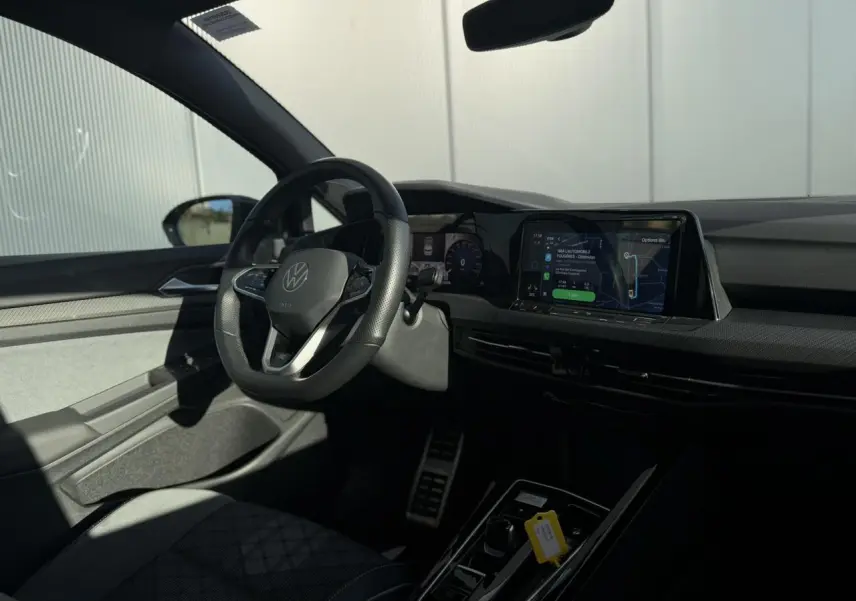 Vue intérieure côté conducteur de la Volkswagen Golf 8 noire avec volant sport multifonction et écran tactile central.