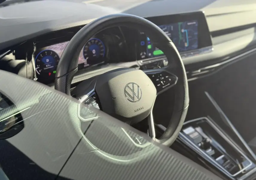 Vue intérieure centrée sur le volant cuir multifonction d'une Volkswagen Golf 8 noire avec tableau de bord numérique et écran tactile.